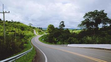 Curved road and long road in rural mountains, green trees, bright green sky.