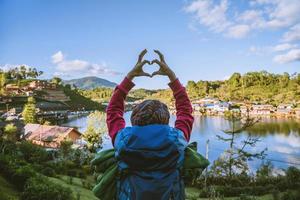 una niña con una mochila disfrutando de viajar en una montaña en el campo. niña feliz con el turismo relajante, levantó la mano para hacer un corazón. foto