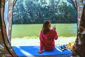 Young woman in the sport wear outfit is sitting and relaxing in the camping in the forest, natural lagoon. photo