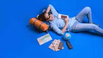 vacaciones de planificación turística con la ayuda del mapa del mundo con otros accesorios de viaje alrededor. mujer viajero durmiendo relajarse en la mano sosteniendo un boleto con un pasaporte sobre fondo azul. mochila de viaje foto