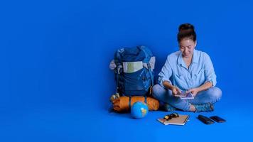 Tourist planning vacation with the help of world map with other travel accessories around. Woman traveler with suitcase on Blue color background. Concept travel backpack