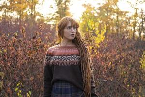 Mujer joven con rastas rojas y vistiendo un suéter en el hermoso bosque de otoño foto