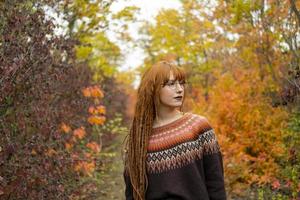 Young woman with red dreadlocks and wearing a sweater in the beautiful autumn forest photo