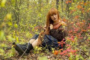 Mujer joven con rastas rojas y vistiendo un suéter en el hermoso bosque de otoño foto