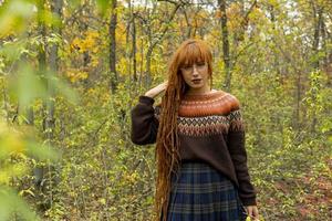 Mujer joven con rastas rojas y vistiendo un suéter en el hermoso bosque de otoño foto