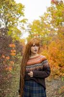 Young woman with red dreadlocks and wearing a sweater in the beautiful autumn forest photo
