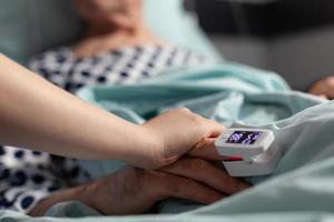 Friendly doctor reassuring sick old patient holding hands photo