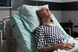 Elderly man laying in hospital room bed wearing cerival collar photo