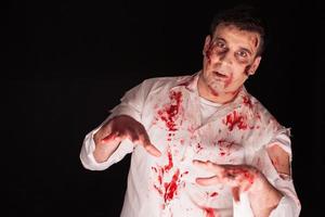 Hombre vestido con un traje de zombie sangriento sobre fondo negro foto