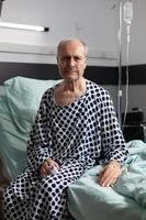 Portrait of sad, unwell senior man sitting on the edge of hospital bed photo
