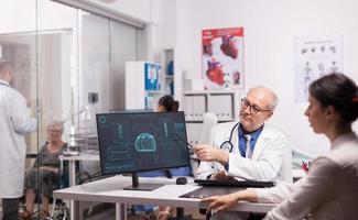 Doctor with grey hair pointing at x-ray photo