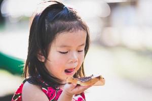 Little adorable girl licking chocolate on lips. Kid with chocolate bread as picnic snack. Baby aged 4 years old. photo