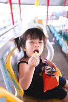 Happy cute 3 year old kid girl eating snacks on grandstand. Child picks up crunchy food in her mouth. Vertical image. photo