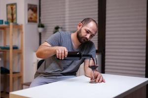 Lonely man pouring wine in glass from bottle photo