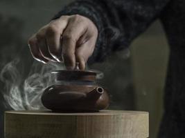 male hand opens the lid of a clay teapot