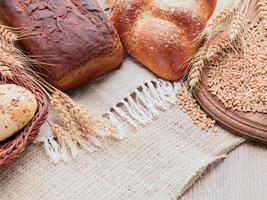 Rye spikelets, wheat bread, bun in the basket. Canvas, burlap, wooden table, wooden cutting board. photo
