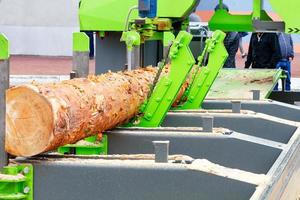 un tronco grande se alimenta automáticamente para serrar en un moderno aserradero para carpintería. foto