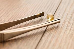 Tablets of fish oil near the tweezers on a wooden table photo