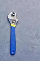 una vieja llave ajustable sostiene una vieja tuerca contra un fondo de hormigón gris. foto