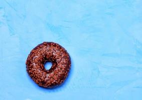 Delicious chocolate donut on a blue concrete surface in cold light. photo