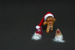 concepto de navidad. Gnomos y hombre de pan de jengibre con gorro de Papá Noel sobre fondo negro con espacio de copia foto