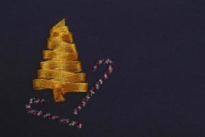 Christmas concept. Golden Christmas tree made of ribbons with a staff on a black background with copy space on top. Template for postcards, packaging, advertising. photo