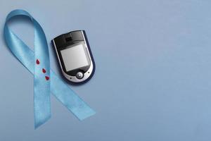 Cerrar la vista superior del concepto para el día mundial de la diabetes el 14 de noviembre. Cinta azul con gotas de sangre y un glucómetro sobre un fondo azul.