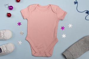 Mockup of New Year's pink bodysuit on a blue background, decorated with white sneakers, red pants and Christmas tree decorations, top view photo