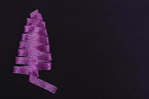 concepto de navidad. árbol de Navidad púrpura hecho de cintas sobre un fondo negro. con plantilla de espacio de copia para postales, embalaje. foto