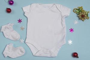 Mockup of a New Year's white bodysuit on a blue background, decorated with white socks and Christmas tree decorations, top view