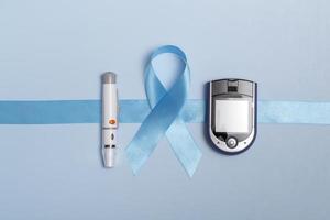 Cerrar la vista superior del concepto para el día mundial de la diabetes el 14 de noviembre. cinta azul con gotas de sangre y un glucómetro sobre un fondo azul. copia espacio
