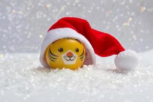 The symbol of the new year is a tiger in a Santa hat on the snow against a background of bokeh lights. Close up of new year photo
