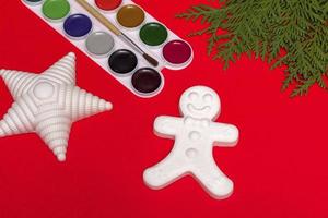 Christmas decorative gingerbread man, star and paints, creativity concept on a red background with a branch of a Christmas tree. With copy space photo