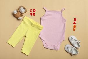 Flat Lay mockup of pink baby shirt, yellow pants, white shoes with toys on a colored background. Layout for design and placement of logos, advertising. photo