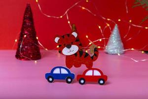 New year minimal concept. Multicolored cars are carrying the tiger - the symbol of the year and multicolored Christmas trees on a pink background. photo