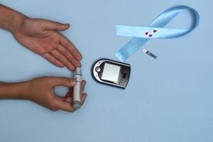 Close up top view of concept for World Diabetes Day 14 November. Child measures blood sugar on a blue background, and a blue ribbon with blood drops. photo