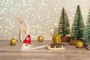 un gnomo con sombrero rojo trajo un regalo dorado en un trineo. fondo de invierno árboles de navidad en destellos y un ciervo. felices vacaciones.