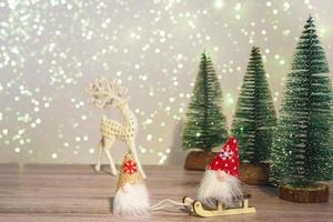 un gnomo con sombrero blanco conduce a un gnomo con sombrero rojo en un trineo. fondo de invierno árboles de navidad en destellos y un ciervo. felices vacaciones.