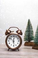 Christmas background with small Christmas trees and vintage alarm clock on a wooden background with lights. Close up Christmas theme. Vertical photo