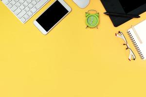 graphic designer desk top view with computer, smart phone, glasses, notebook, and time clock on yellow background photo