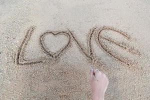 woman hand doing heart symbol and love word handwritten on sandy beach photo