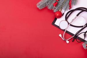 Portapapeles con estetoscopio médico, gafas, árbol de navidad sobre fondo rojo con espacio de copia