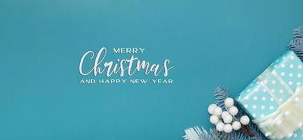 Feliz navidad saludo banner con regalo de navidad plano laico, bayas y fondo turquesa de pino foto