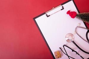 Clipboard with medical stethoscope, glasses, christmas tree on red background with copy space photo