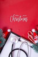 Feliz navidad saludable texto con estetoscopio médico y adornos navideños sobre fondo rojo. foto