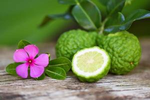 Fresh bergamot fruit and pink flower Kaffir Lime Citrus bergamia with leaf on wooden table Slice bergamot citrus fruit essential oil concept. photo