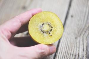 rodaja de kiwi sobre fondo de madera, kiwi en mano. foto