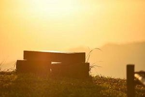 nature warm light with wooden bench on grass meadow with sunrise or sunset on the mountain background. photo