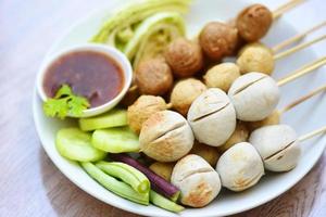 Meatballs on skewers on white plate and fresh vegetables cabbage yard long bean cucumber, Asian Thai food grilled meatballs fishball and porkball with picy sauce photo
