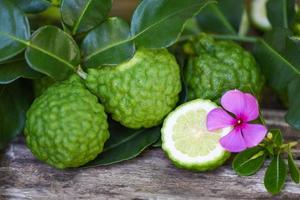 Fresh bergamot fruit and pink flower, Kaffir Lime, Citrus bergamia with leaf on wooden table, Slice bergamot citrus fruit essential oil concept. photo